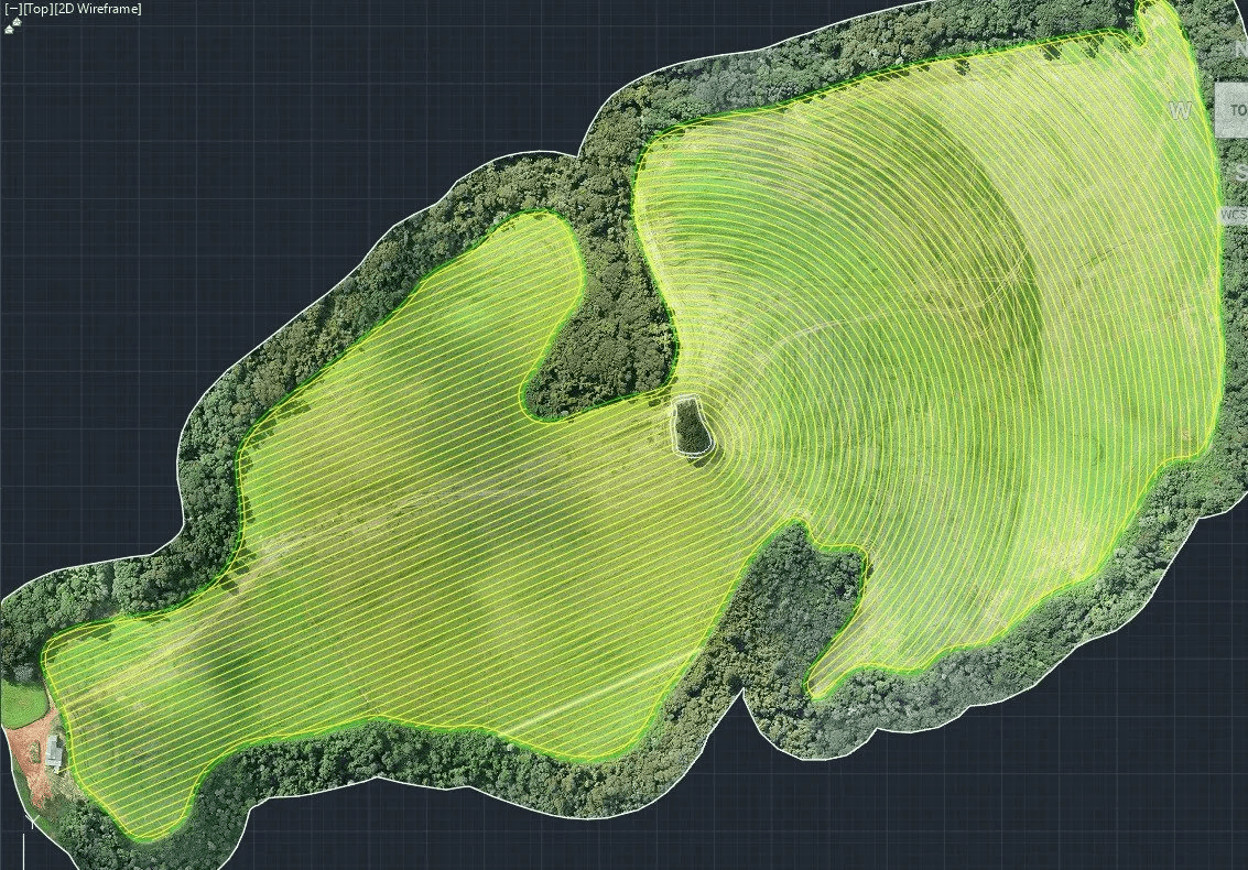 Aerial view of a contoured green agricultural field bordered by lush forest.